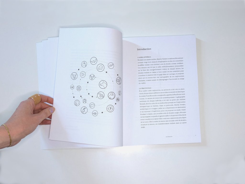 A hand turns the pages of the open book. The left page shows a circular diagram of small icons arranged in a spiral, the right page is headed "Introduction" with French text below.