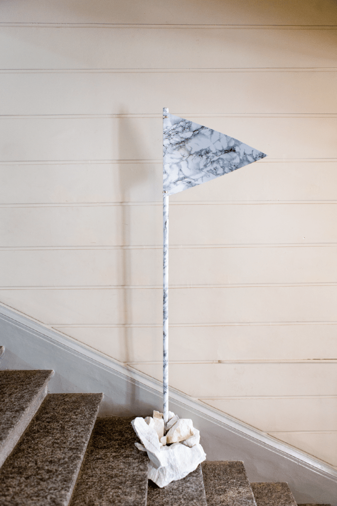 476 Promises (Distinction), 2017 
Carrara marble stones, self-adhesive marble imitation plastic foil, flag staff, 200 cm, cable binders
Exhibition view: 47.2120991° N 7.7892601° 